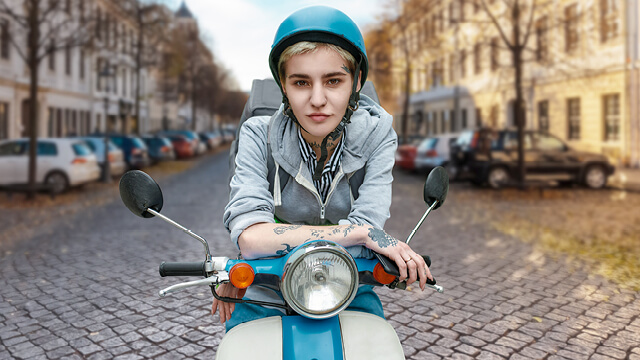 Mopedversicherung: Eine junge Dame sitzt auf Vespa und hält einen weißen Helm in der Hand