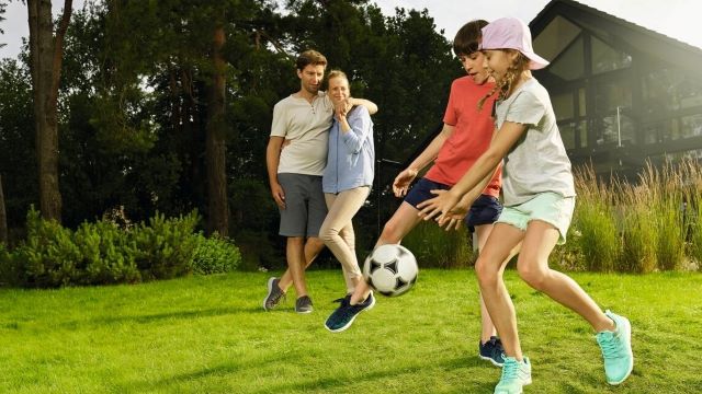 Private Haftpflichtversicherung: glückliche, entspannte Familie. Kinder spielen Ball, Eltern beobachten die Kinder.