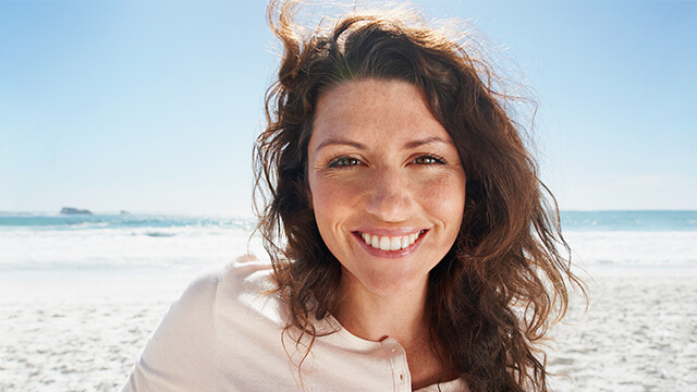 Reiserücktrittsversicherung: Eine lächelnde Frau erholt sich in ihrem Urlaub am Meer.