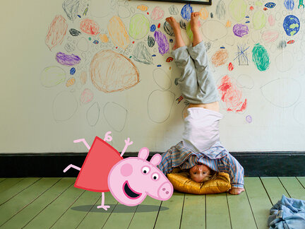 Ein Kind steht auf den Händen auf einem Kissen, während bunte Kritzeleien an der Wand hinter ihm sichtbar sind. Peppa Wutz ist als Cartoonfigur daneben.