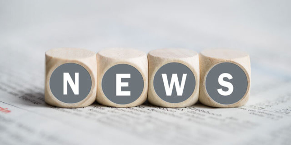 Holzklötze mit den Buchstaben N, E, W, S auf grauem Hintergrund, die das Wort "NEWS" bilden.