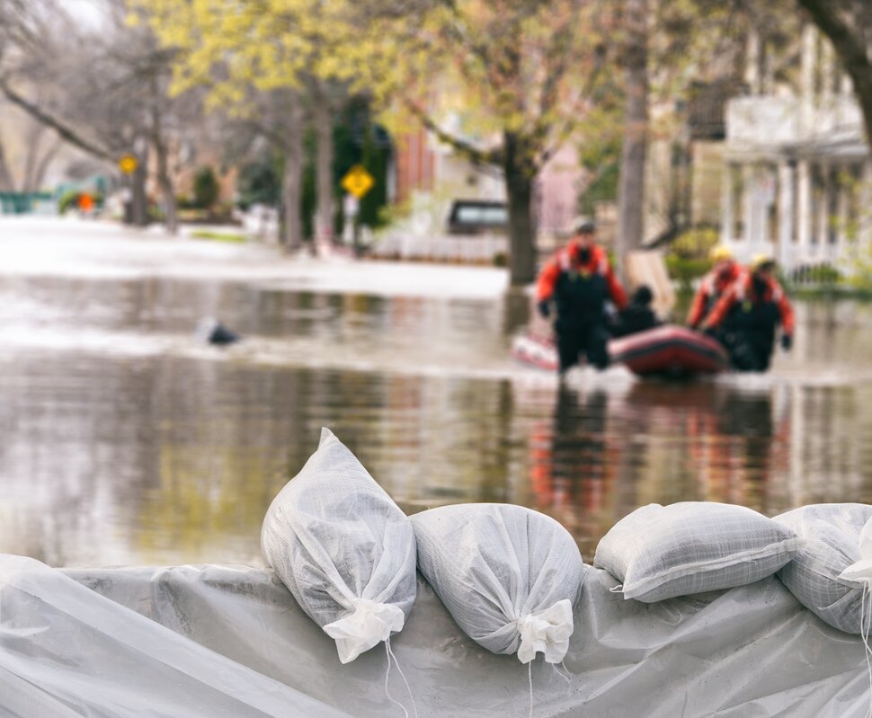 Sandbags schützen vor hochrangigem Wasser, während Rettungskräfte in einem Schlauchboot durch überflutete Straßen fahren.
